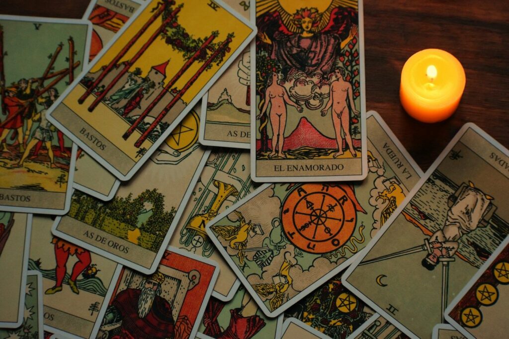 A lit candle beside a pile of Rider-Waite-Smith tarot cards, with The Lovers and the Wheel of Fortune on top