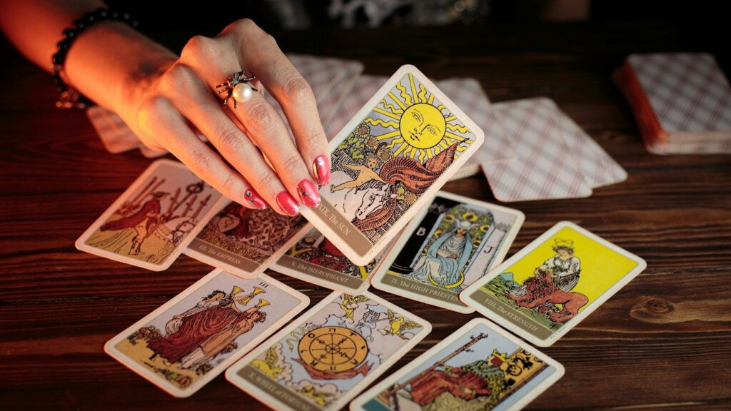A hand laying Rider-Waite-Smith tarot cards on a wooden table, with The Sun, The High Priestess, Strength and the Wheel of Fortune face up